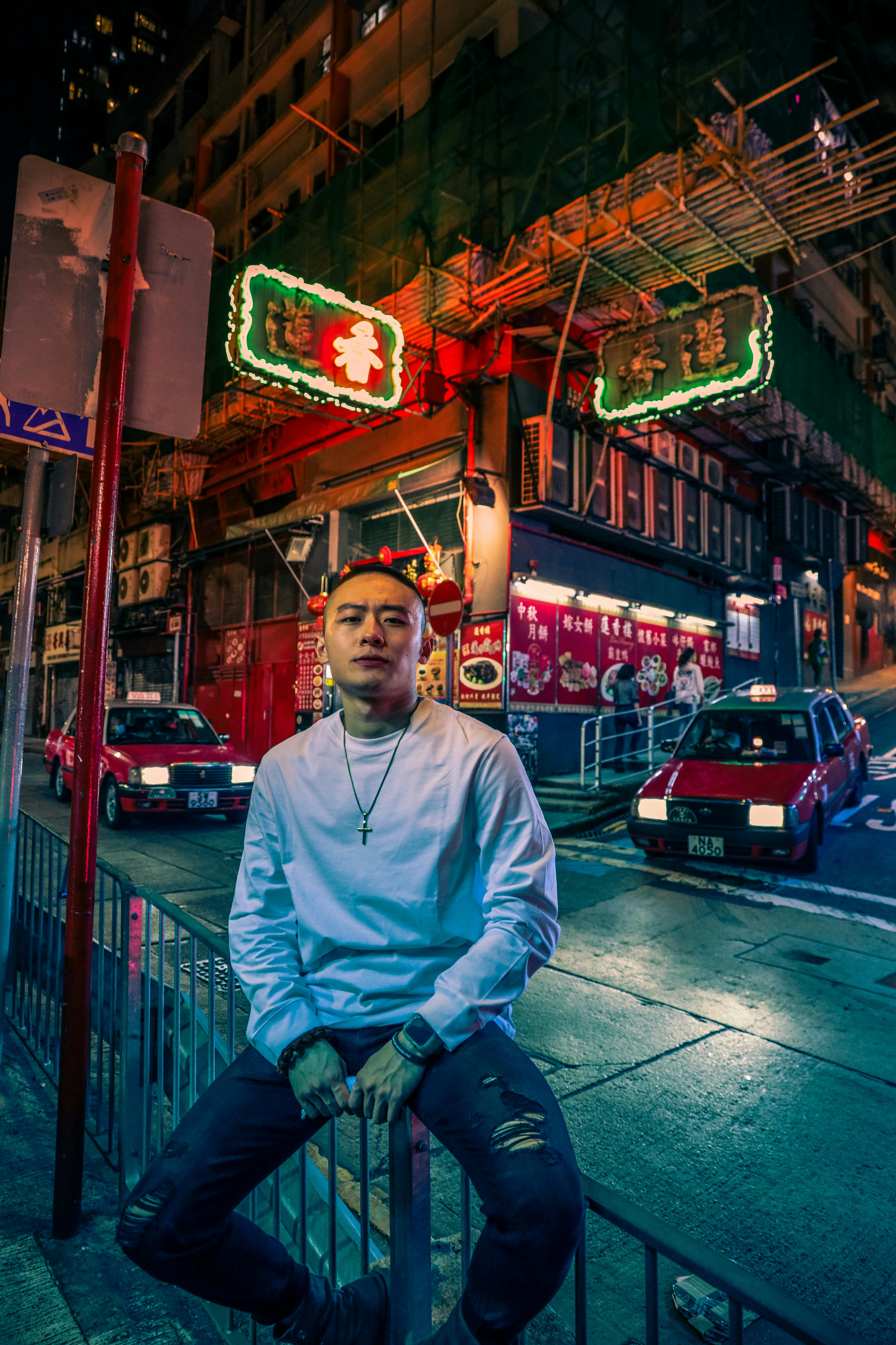 man in white sweater sitting on red metal fence during night time
